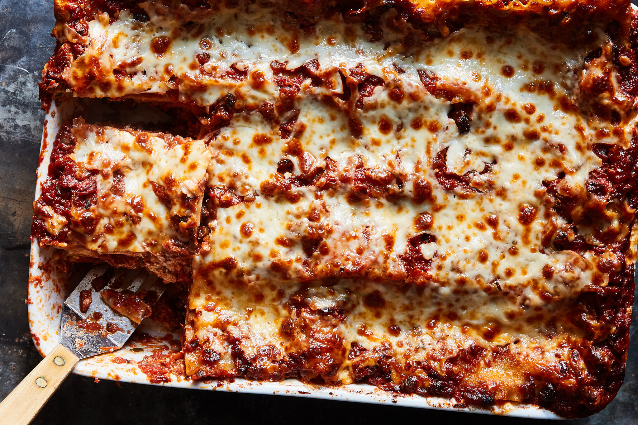 Overhead view of lasagna in a white baking dish with slices removed, showcasing portion control for efficient cooling and refrigeration, ideal for food safety and meal prepping.