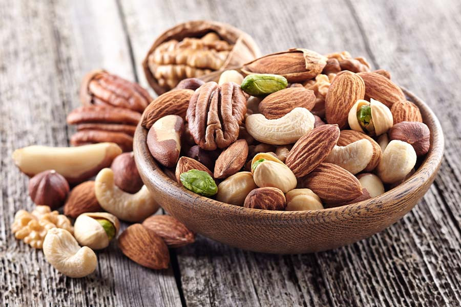 Variety of mixed nuts including almonds, walnuts, and pistachios displayed in a wooden bowl, highlighting healthy fats and protein sources for muscle growth.