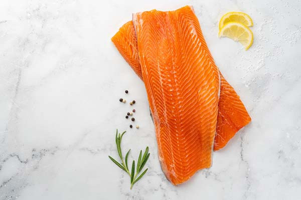 Raw lake trout fillets prepared with lemon slices, rosemary, and peppercorns, highlighting a delicious and healthy source of omega-3 fatty acids for a balanced diet.