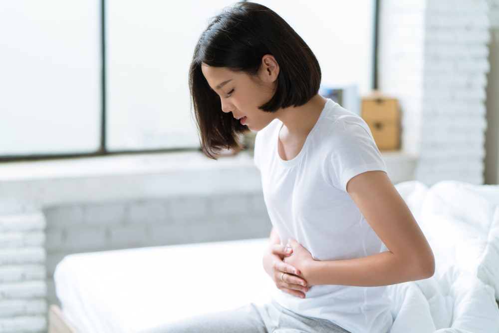 Woman experiencing stomach pain from constipation, a symptom of slow digestion.