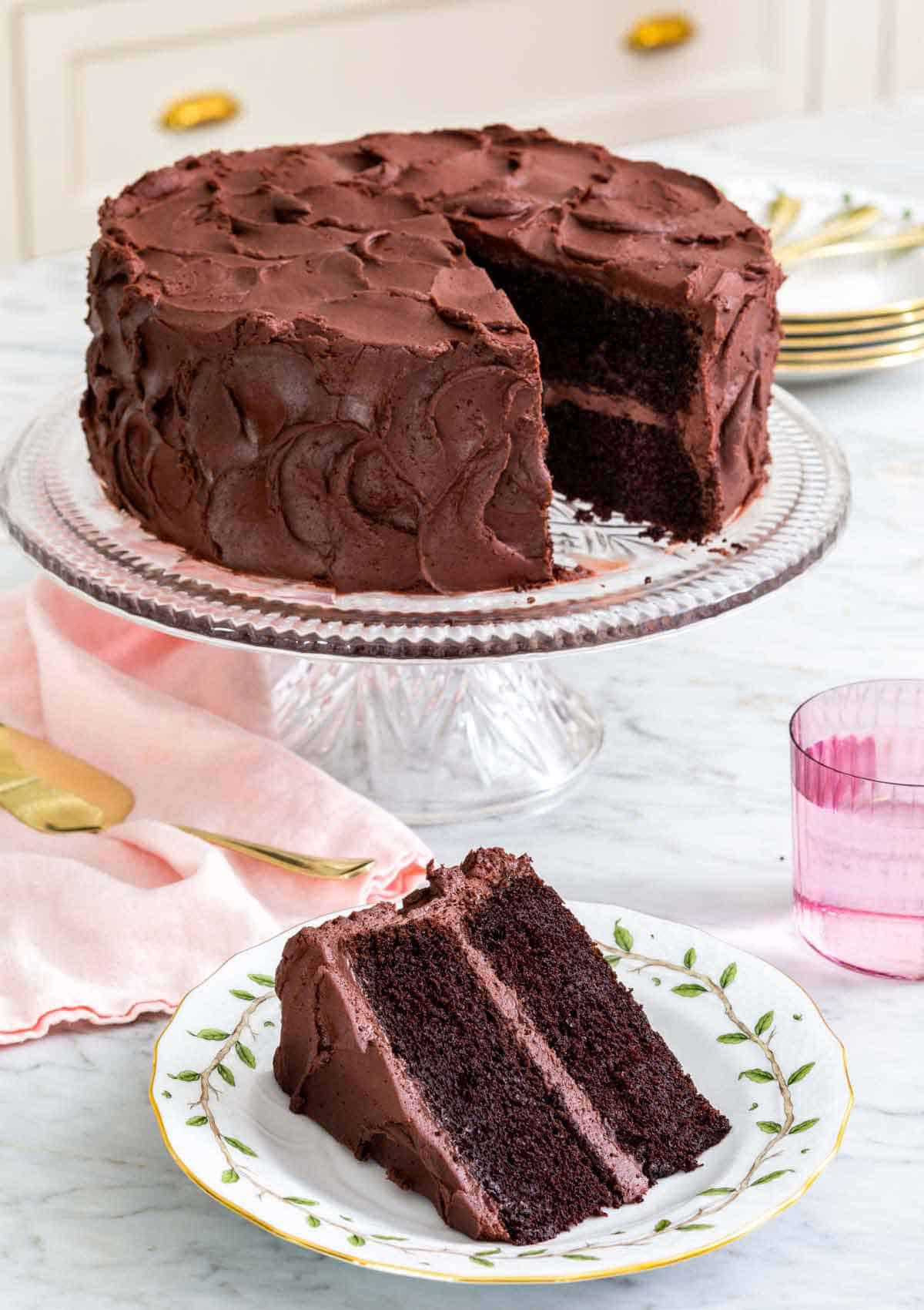 A finished devil's food cake on a cake stand with a slice removed.