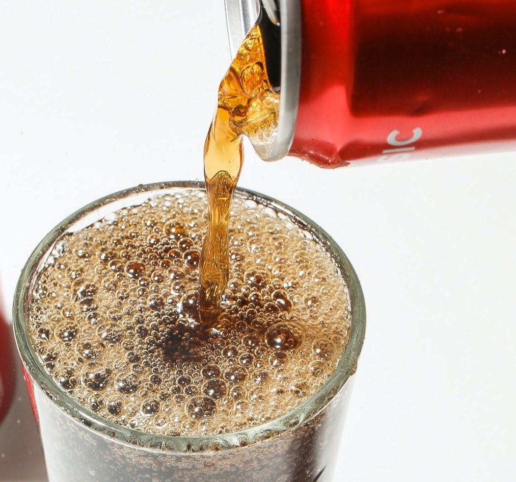 Pouring soda into a glass, representing processed beverages high in inorganic phosphorus additives.