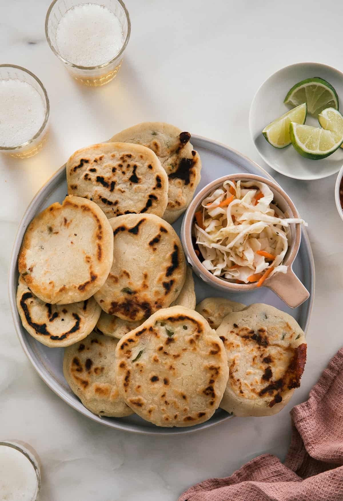 Pupusas on a round plate with curtido and limes, showcasing authentic Salvadorian food.