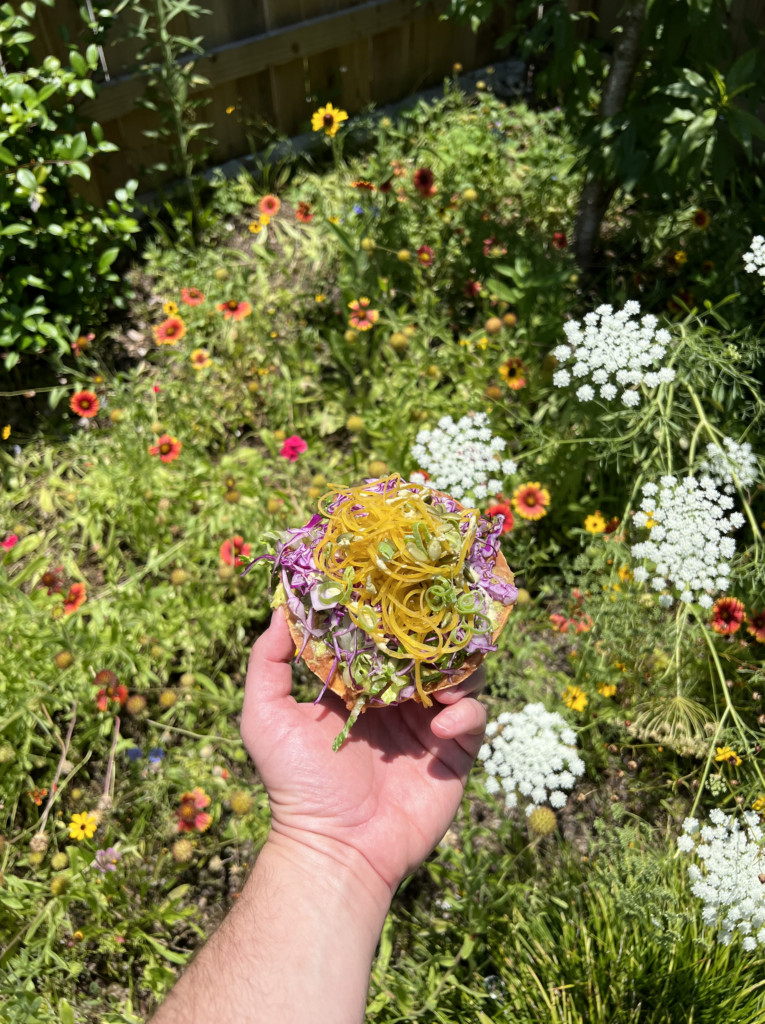 Rainbow tostada held over a colorful garden