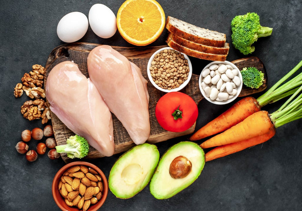 A colorful assortment of niacin-rich foods including chicken breast, beef steak, salmon fillet, brown rice, lentils, peanuts, sunflower seeds, and bananas, displayed on a wooden surface to illustrate diverse dietary sources of vitamin B3.