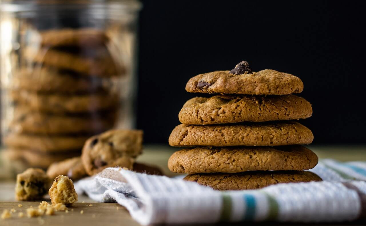 Stacked chocolate chip cookies with a cookie jar behind them.