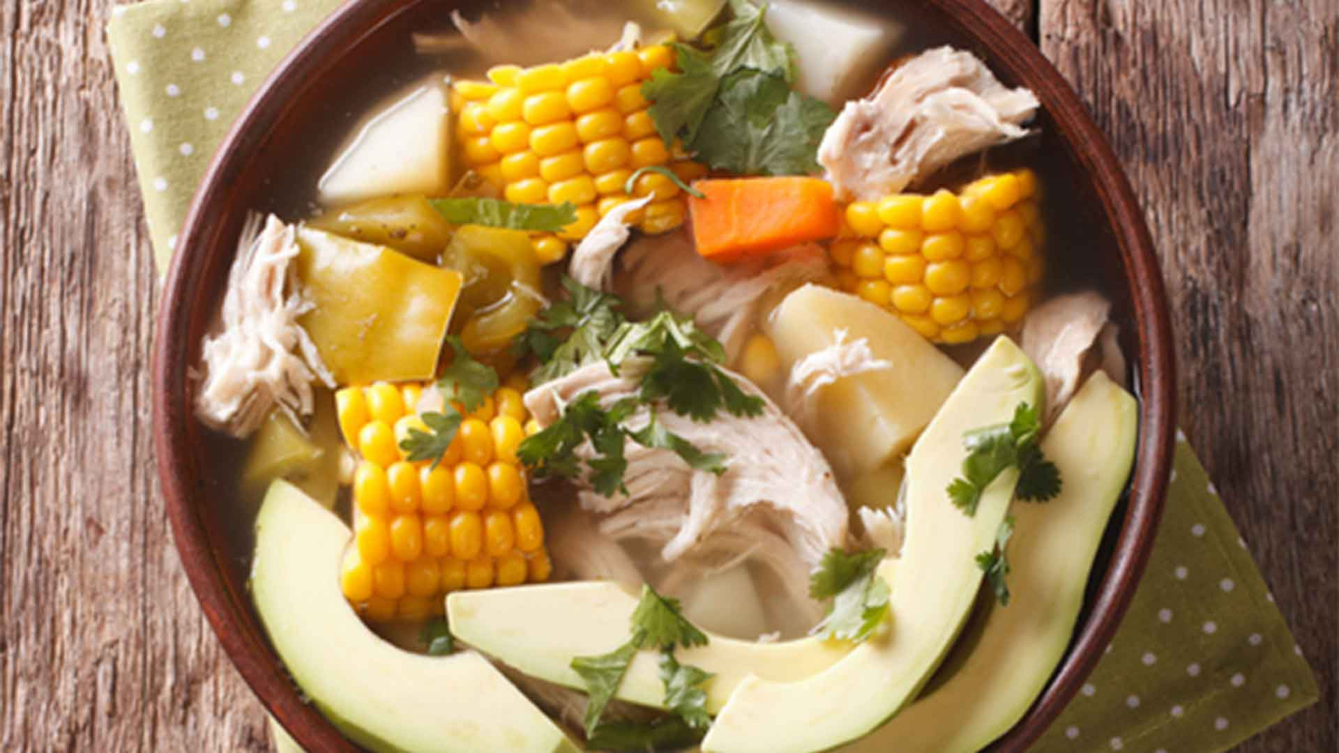 A creamy bowl of Colombian Ajiaco soup, made with three types of potatoes, chicken, cream, capers, and guascas herb, showcasing its distinctive taste and texture, garnished with fresh cilantro and avocado slices.