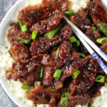 A close up of a plate of food with cooked thinly sliced steak tossed in Mongolian beef sauce.