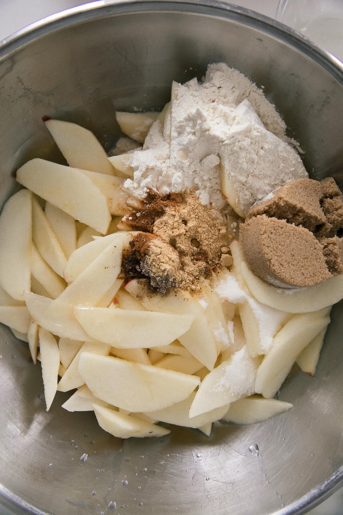 Sliced apples being mixed with spices and sugar to prepare the apple cobbler filling, showcasing the ingredients and initial steps of the recipe.