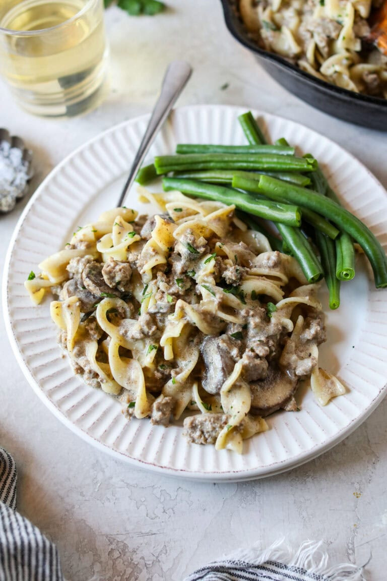 Overhead view of a plate of ground beef stroganoff with a side of fresh green beans topped with fresh herbs.