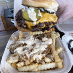 Close-up of a person holding a juicy smash burger from Seattle's Smash That food truck, known for its thin, crispy patties and flavorful caramelization.