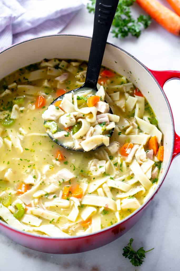 A ladle scooping homemade chicken noodle soup