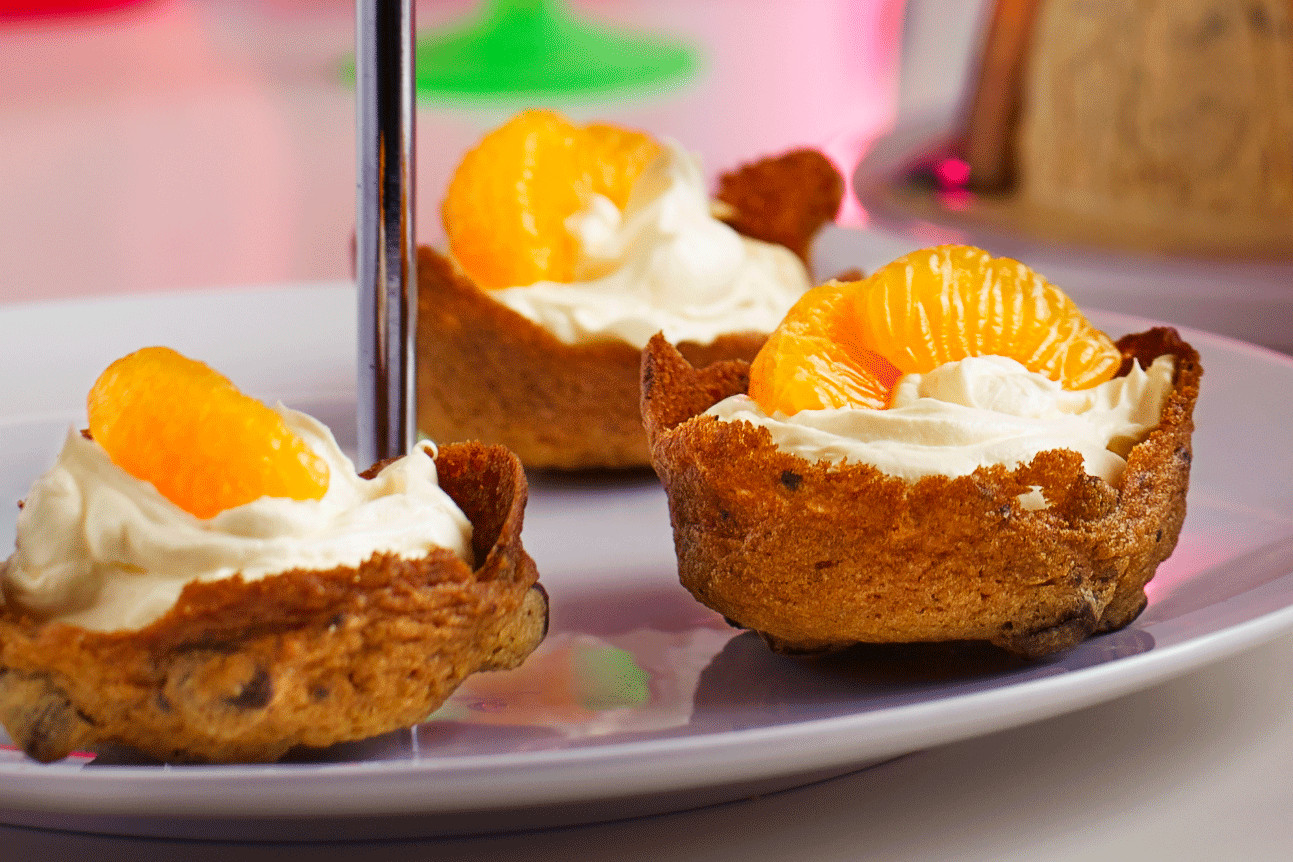 Mandarin slice on top of a mini cookie cup filled with orange and mandarin cream on a cake stand