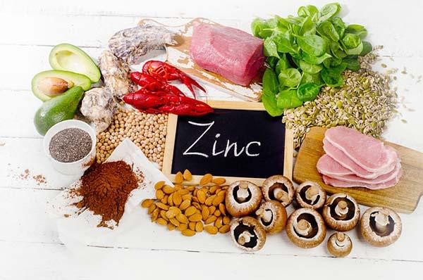 An assortment of foods high in zinc, including beef, avocado, lentils, mushrooms, pumpkin seeds, and almonds surrounding a small slate with the word zinc written in chalk. The image shows a variety of zinc-rich foods alongside the word "zinc" written in chalk, emphasizing the importance of dietary sources of this essential mineral