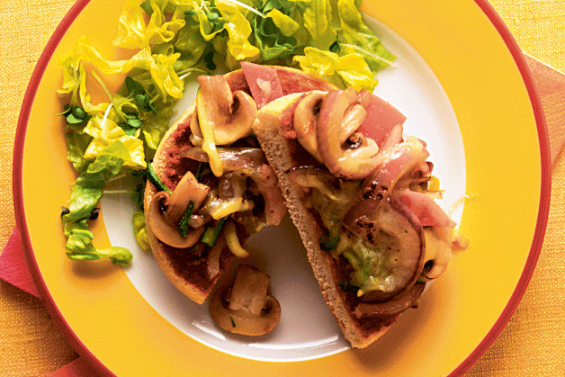 Mushrooms, ham & cheese on an English muffin on a yellow plate with salad leaves