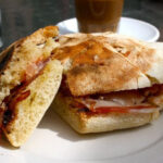 A toasted, halved sandwich on a white plate, with thinly sliced cured ham in the middle.
