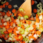 Soffritto of onions, carrots, and celery cooking in a pot, essential for minestrone's flavor base